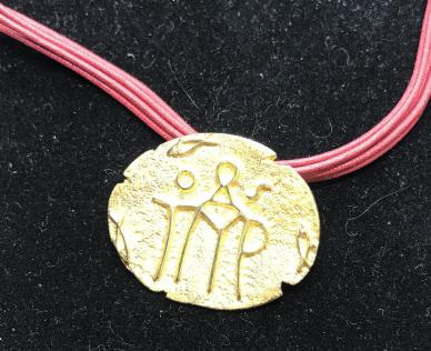 Aboriginal Motif Pendant/Brooch: Gold Tone Metal, hammered finished with aboriginal stick figure design in relief. Contrasting red cord. Spring ring clasp. Pendant changes to use as a pin, brooch. Measures app 1 1/4 x 1 in. Cord leng