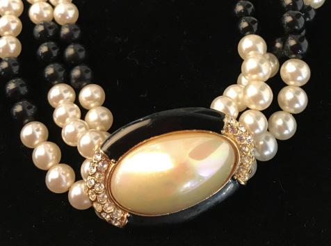 Triple Strand Choker W Cabochon Pendant: Alternating lengths of white & black fashion pearl style beads on three strands. Large oval center pearl style cabochon (1.5 x 3/4 in.), bezel with black enamel and rhinestones, Gold tone metal finish