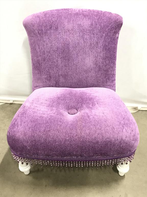 BOMBAY & CO Low Beaded Purple Chair: Tag on underside reads BOMBAY KIDS along with additional information. Chair has light purple tone upholstery & has 1 button tuft on seat. Chair has white tone carved wooden feet. Lower edge of piece h