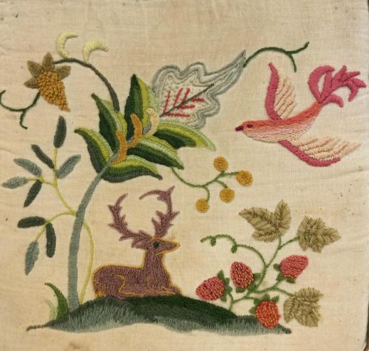 Vintage Needlepoint Embroidery Toss Pillow: Vintage possibly antique, off white toned fabric with green and brown trim, multi colored embroidered design, bright pink flying bird, purple sitting deer and art Nouveau inspired floral scene, foam i