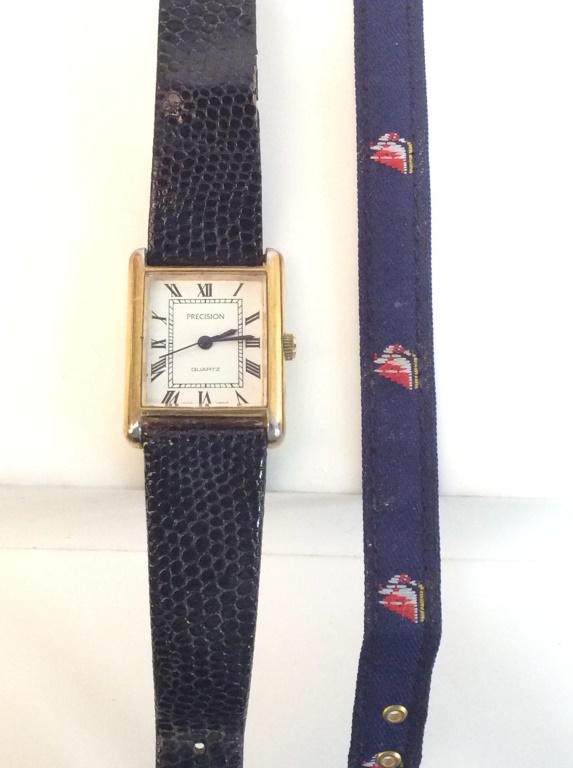 PRECISION Rectangular Wristwatch: In the style of the Cartier Tank Solo Wristwatch. Gold toned watch head with Roman numerals, stainless steel back and base metal bezel. Watch head measures 1 1/8 x 7/8 in. Pebble black leather strap, 