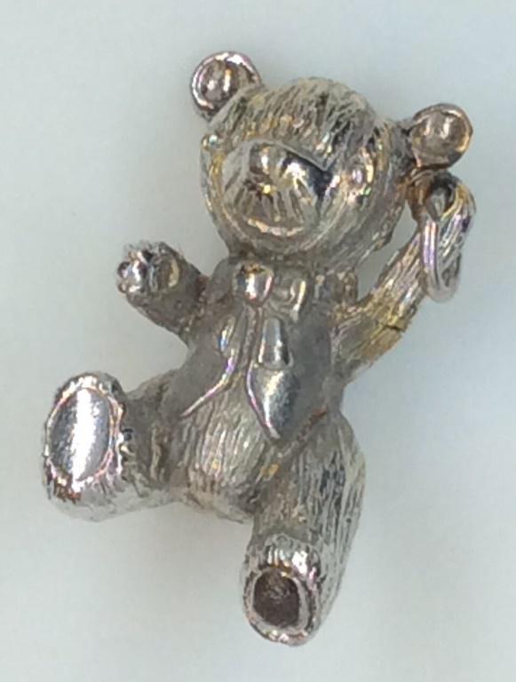 TEDDY BEAR CHARM/PENDANT: Teddy bear dressed in vest and bow tie. Bale attached to be used as a charm on a bracelet or a pendant on a chain or rope. Bale is on top corner, will hang on an angle. 1 in long. Silver tone etched m