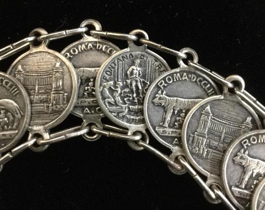 Ancient Roman Iconic Coin Bracelet, jewelry: 18 dime sized coins, 17 set in long link chain. Spring Ring needs replacing. Additional charm coin at clasp. Two sided metalwork in relief. Coins depict Romulus & Remus with She-Wolf, The Trevi Founta