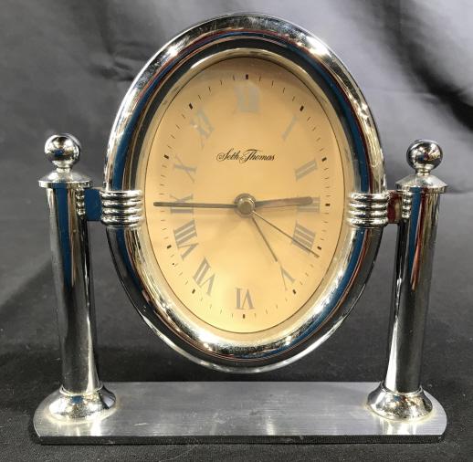 SETH THOMAS Silver Toned Desk Clock: This is a SETH THOMAS Silver Toned Clock. The base and support arms are crafted from metal, the housing of the clocks face appears to be plastic. The piece measures approx 5.4 inches H, and 5.6 inches