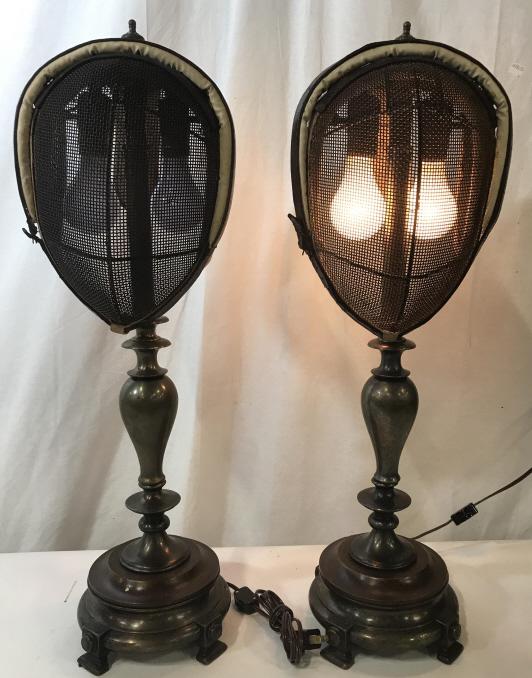 ‘Jewelry St. Art,’ pair Fencing Mask Lamps: Two Way Lighting, low & high. Vintage fencing protective masks converted into lamp shades for a one of a kind avant- guard Lighting experience. App 27 in. Ht, 9 in. width. Both with finials. Footed gu