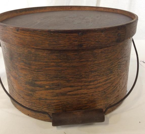 Vintage Hand Formed Round Wood Box: Metal carry handle with wood grip. Possibly used as a sewing box, hat box or for stored commodities. Metal rivet nails, bottom with plank wood, lid’s center wood top loose in rim. Possibly antique, 