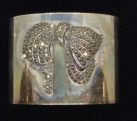 Sterling Silver W Marcasite Wide Cuff, 38.8 dwt: Marcasite bow dimensional design on surface. Labeled 925 and copyrighted with C inside a circle stamp. Additional hallmark, back to back triangles. 1 3/4 in. wide. 1 1/4 in opening. Sterling Silver, 9