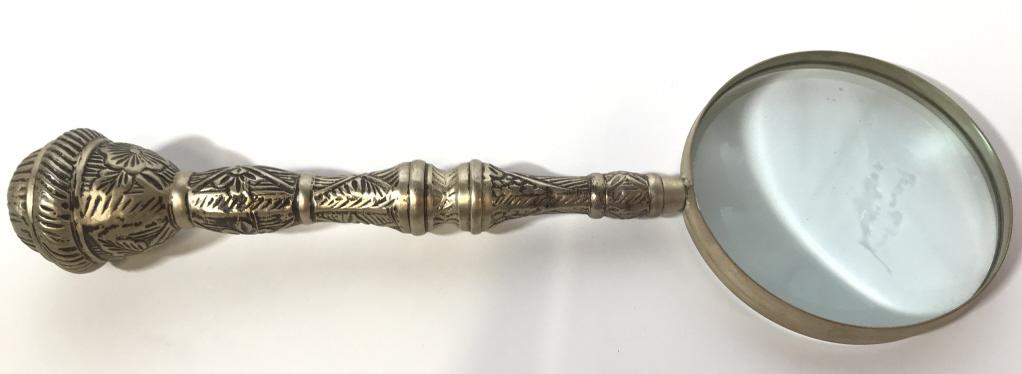 Vintage Silver Toned Metal Magnifying Glass: Magnifying glass handle is silver toned and metal, possibly silver plate. Contains geometric and floral relief detail piece measures approximately 12 inches tall 4 inches wide at head. Vintage magnify