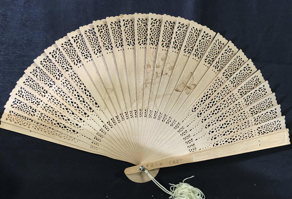CAAC Wooden Handheld Fan: This is a wooden fan distributed by CAAC, the Civil Aviation Administration of China. The fan has a tassel attached, and is features illustrations of plants and a butterfly on the ribs of the fan. The