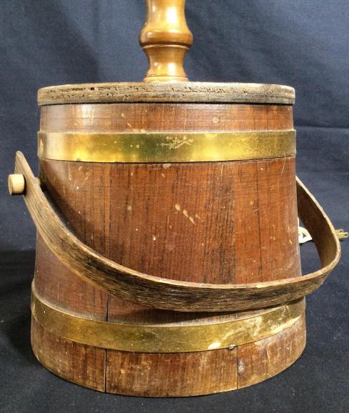 Vintage Wooden Bucket Lamp: This piece is a vintage lamp, the base is crafted from a wooden bucket. The bucket is held together by brass clamps and rivets. The buckets handle displays some level of articulation. The piece measur