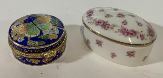 Lot 2 vintage Pill boxes: Trinket boxes are unmarked. Circular box has a butterfly design on top. Oval shaped trinket box has a rose pattern. Circular box has a clasp closure. Oval shaped box is lidded. Small crack on rim. Bot