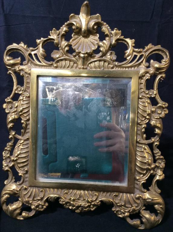 French Bronze Dresser Top Mirror: Brass Over bronze, ornate vanity/ valet/ dresser mirror with stand attached. Pierced & embossed metal work. Fleur de lis crest over scallop sea shell, florals, scrolls. App 14 x 11 in. Beveled mirror,