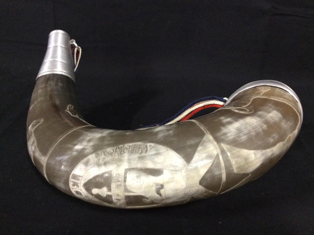 Republic Of Paraguay Ox Horns: This is a pair of ox horns, both pieces are capped with metal. The larger horn has had a red, white, and cblue strap attached to its metal caps. The larger horn features carvings of serpents, goat, an