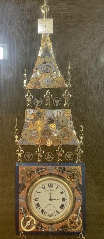 Framed Horological Clock Tower Art: This piece is a framed clockwork collage from. The piece is assembled from gears, coils, and clock faces. The pieces have been rearranged to resemble a Clock tower. The piece measures approx 16 inches