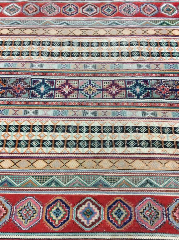 Vintage Handmade Moroccan Room Size Wool Rug: Rug is wool and handmade. Piece is vintage possibly antique. Underside has tag which reads ARTISANAT MOROCCO. Rug contains multi toned geometric detail. Rug is Fringed. Some areas of rug have thicker 