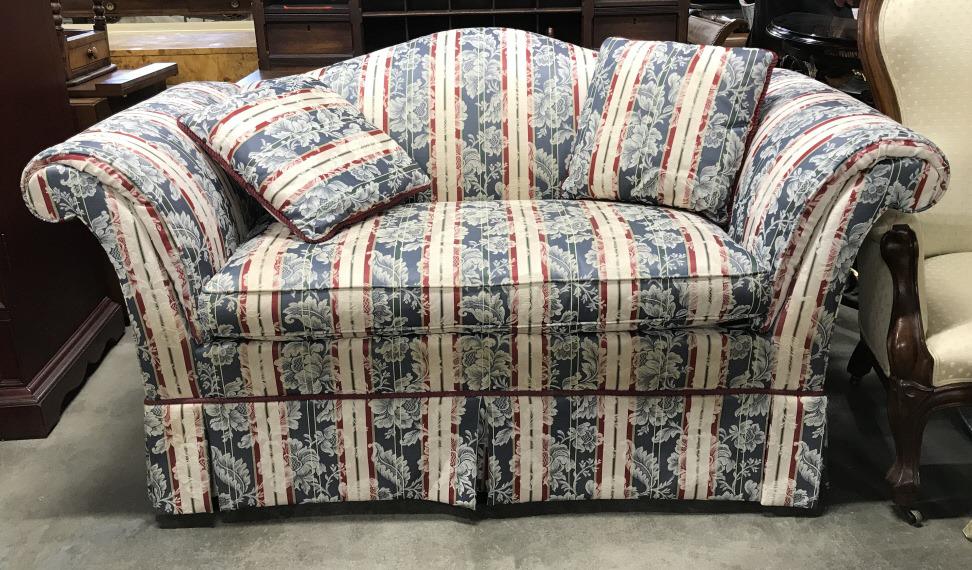 BEACHLY Skirted Love Seat: Love seat has tag which reads BEACHLY. Piece has multi toned striped detail with tones of red, green, gold and cream. Piece also has floral leaf and vine detail. Sofa is Skirted. Piece measures approx
