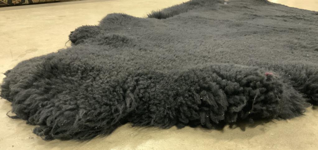 Black Sheepskin Throw Rug Carpet: This is a black sheepskin throw rug. The underside ha been colored an eggplant or plum tone. The rug shows some signs of wear due to its use. Rug measures approx 45 inches long and 39 inches wide. Rug