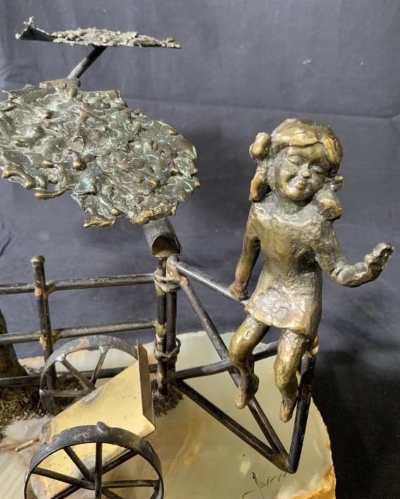 Signed Bronze & Quartz Youth Tree Sculpture: This a bronze sculpture mounted to a quartz base. The piece is signed illegibly. The piece depicts a young girl sitting on a fence, a wheel barrow sits in front of the fence, a tree hangs overhead. Th