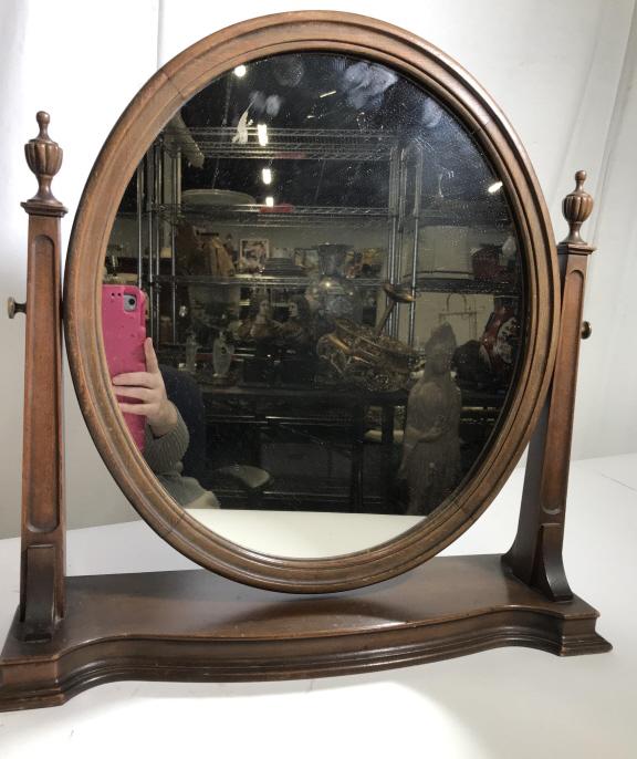 Vintage Dresser Top Mahogany Swivel Mirror: Oval Mirror on stand, possibly antique, mahogany wood. Mirror pivots up and down. Neoclassical columns flank mirror o stand. Piece measures 19.5 in wide, 19 in. tall, 6 in. deep. Mirror Measurements 1