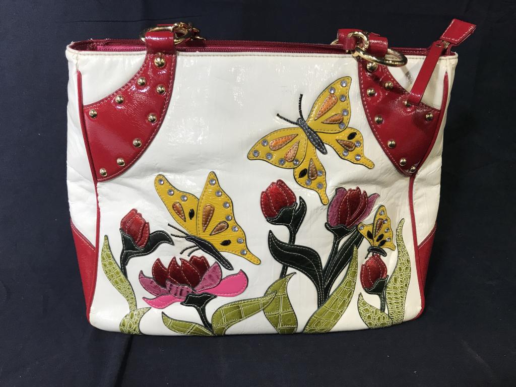 Sharif 1827 Couture Handbag: Appliqué Flowers and butterflies on front panel, cream bad with genuine leather red trim. Texture mimics that of patent leather. Gold tone hardware braided to handles and gold tone stud design. Under