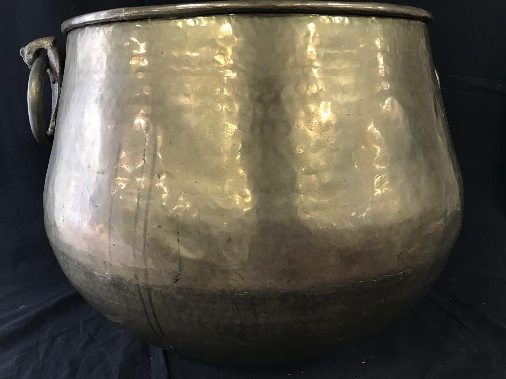 Oversize Brass Firewood Bucket w/ Ring Handles: Shabbiria Arts Hammered Brass firewood holder. Solid brass ring handles attached to decorative griffin. Cauldron shape, rounded piping top rim. India. 25 in. wide by 16 in. tall. Opening 18 in. wide. 