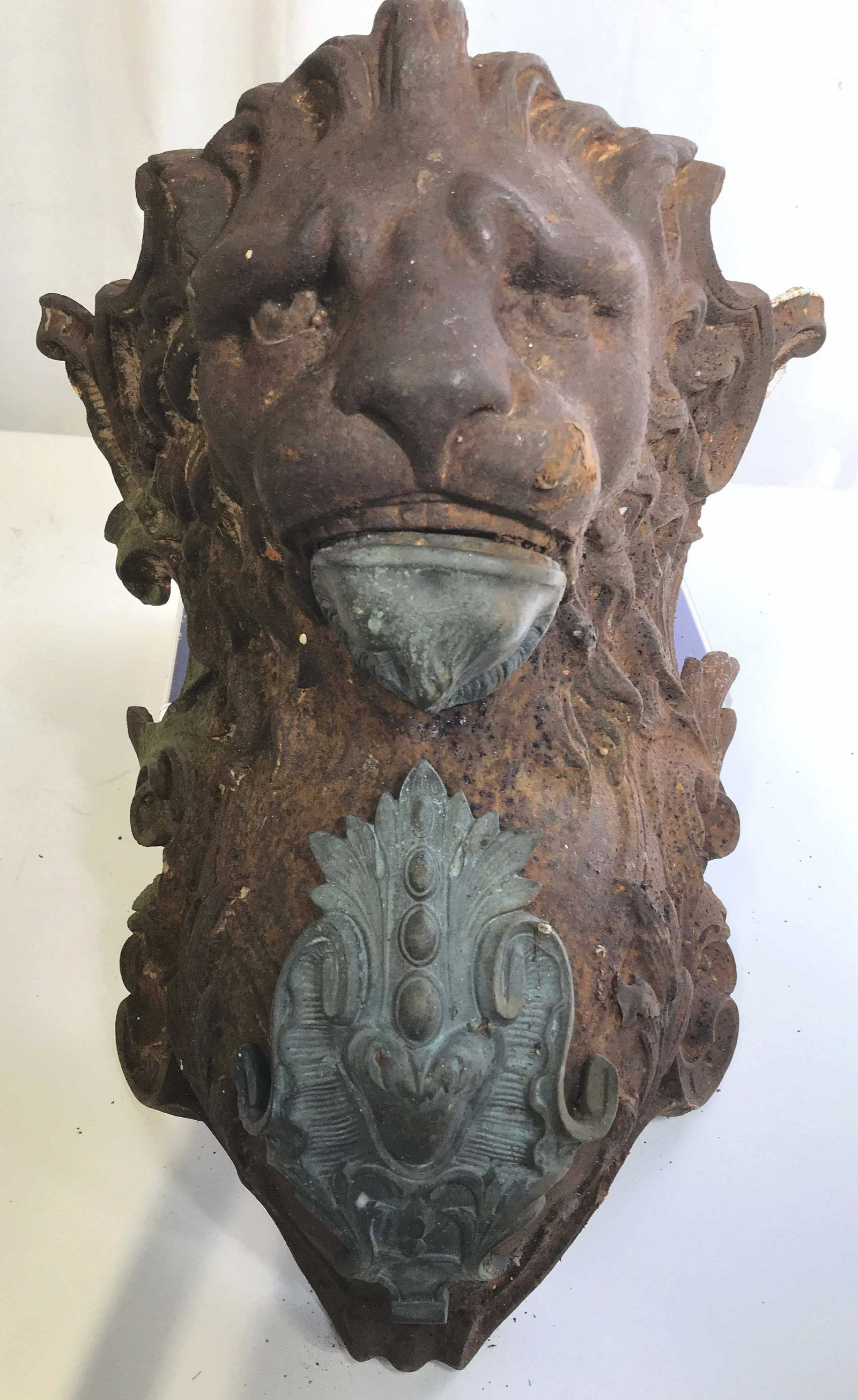 Antique Iron & Bronze Lion Head Sculpture: Neoclassical Scroll & crest design lion head griffin/ sculpture, possibly antique. Rusted surface, but solid metal & Extremely heavy piece. Mixed metals. Lion head bolted to supportive iron brackets. 
