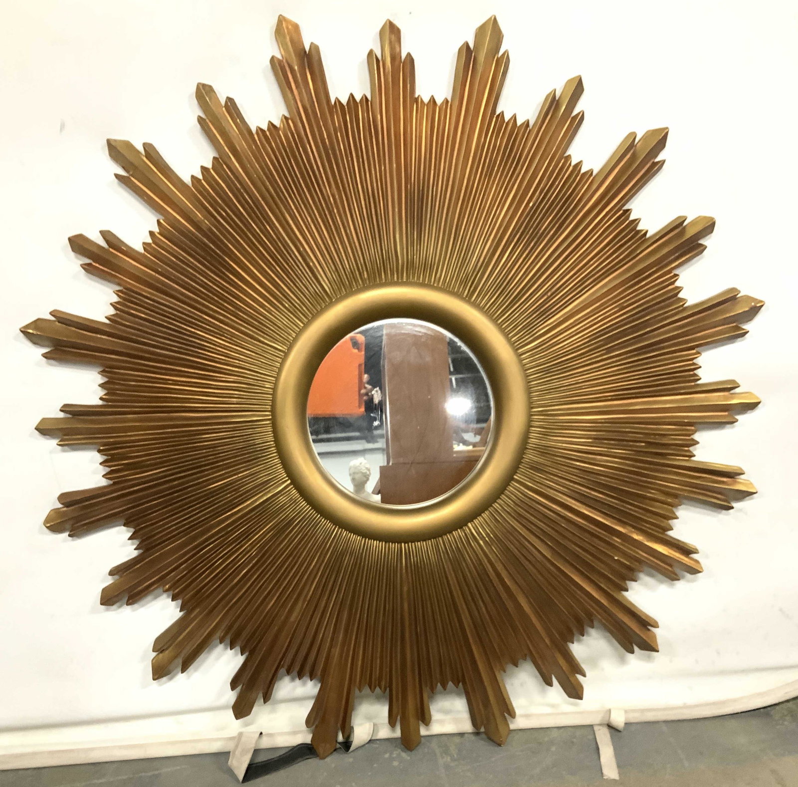 THE UTTERMOST CO Gold Toned Sunburst Wall Mirror: Backside is marked THE UTTERMOST COMPANY. Wall mirror is gold toned. Piece has large sunburst frame. Mirrored surface is circular. Frame appears to possibly be composite & possibly is gold leafed. Pie