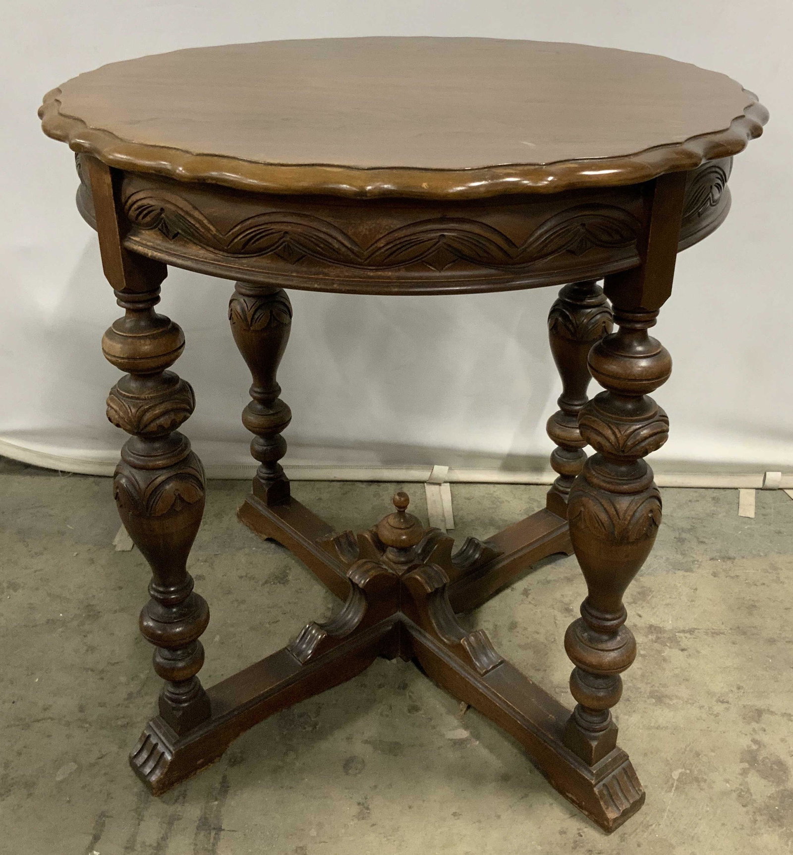 Antique Carved Wood Side Table: This is an antique side table. The piece is walnut toned, the legs are turned, and detailing has been carved into them. The four legs are joined by an X-shaped stretcher, a finial can be found at the 