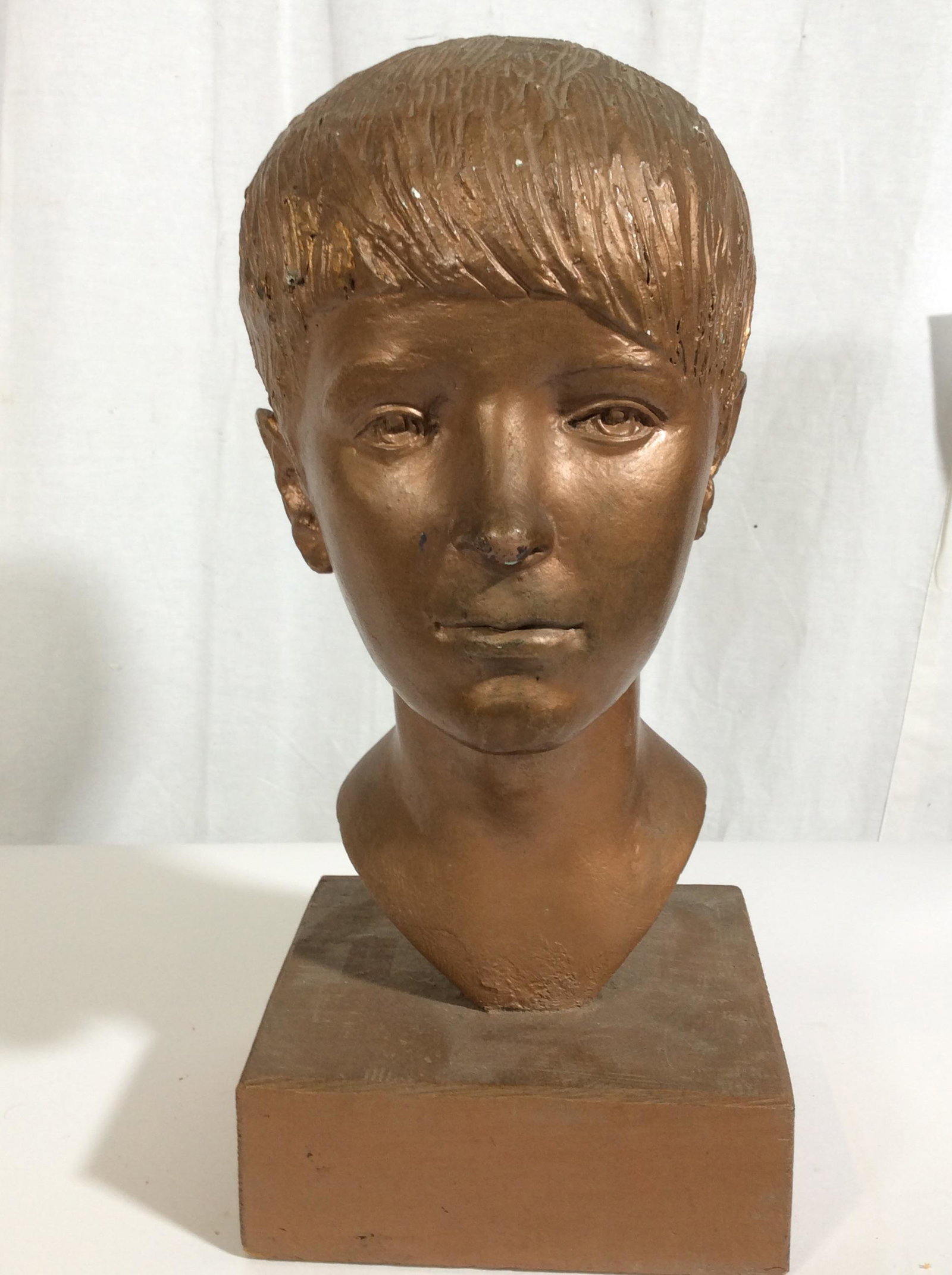 Floor Size Vintage Plaster Child Bust: This piece is a vintage bust. The piece has been crafted to resemble a boy. The piece is colored in copper tones. There is some wear present on the piece, the wear is consistent with age and handling.