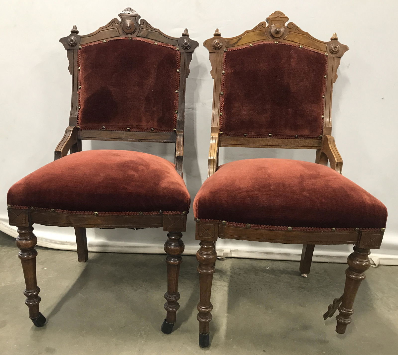 Pair East Lake Wooden Victorian Style Side Chairs: Side chairs are vintage possibly antique. Each chair has deep red toned upholstery upholstery. Piece has intricately carved wooden detail. Edges of upholstery have gold toned nailhead detail. Some are