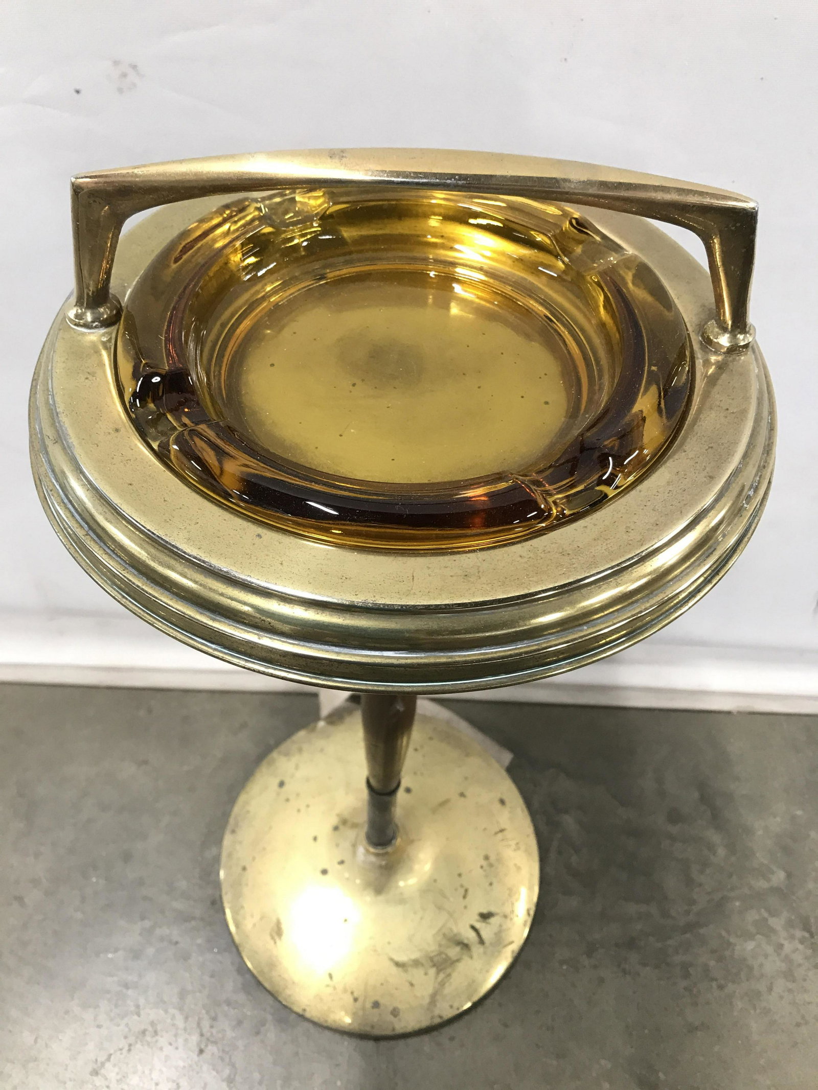Vintage Gold Toned Metal Ash Tray Table: Ash tray table is gold toned. Piece includes clear & amber toned glass pieces at top. Top also has gold toned metal handle. Piece measures approximately 27 inches tall 11 inches wide. May need structu