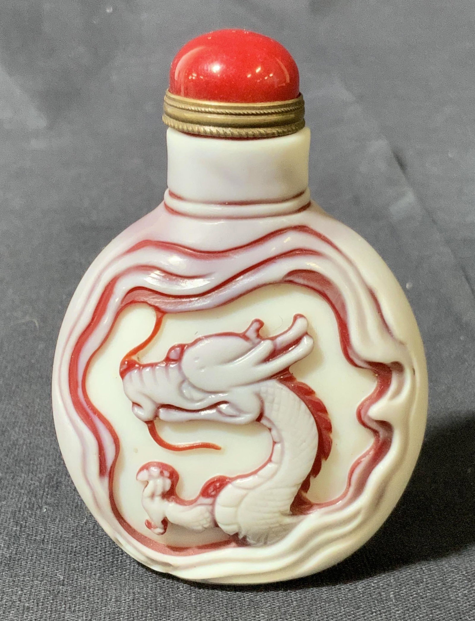 Vintage Glass East Asia Snuff Bottle: This is a vintage, possibly antique, East Asian snuff bottle. The piece appears to crafted from glass, and features a dragon on each side, in relief. The glass is ruby and milk toned. The cap is craft