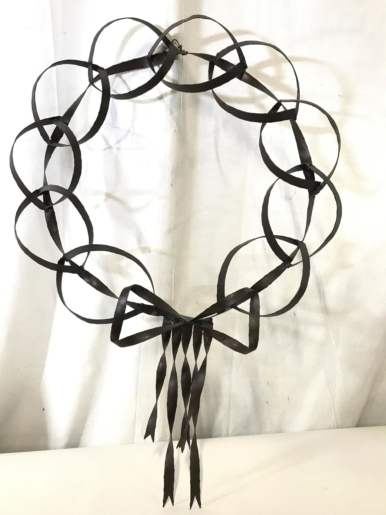 Metal Art Wreath Wall Sculpture: Original Art, hand Formed metal craftsmanship, wreath created by loop links with bow and ribbon. Measures 27 in. wide, 38.5 in. long. Has hanging wire attached. One loop link is loose. Industrial Art,