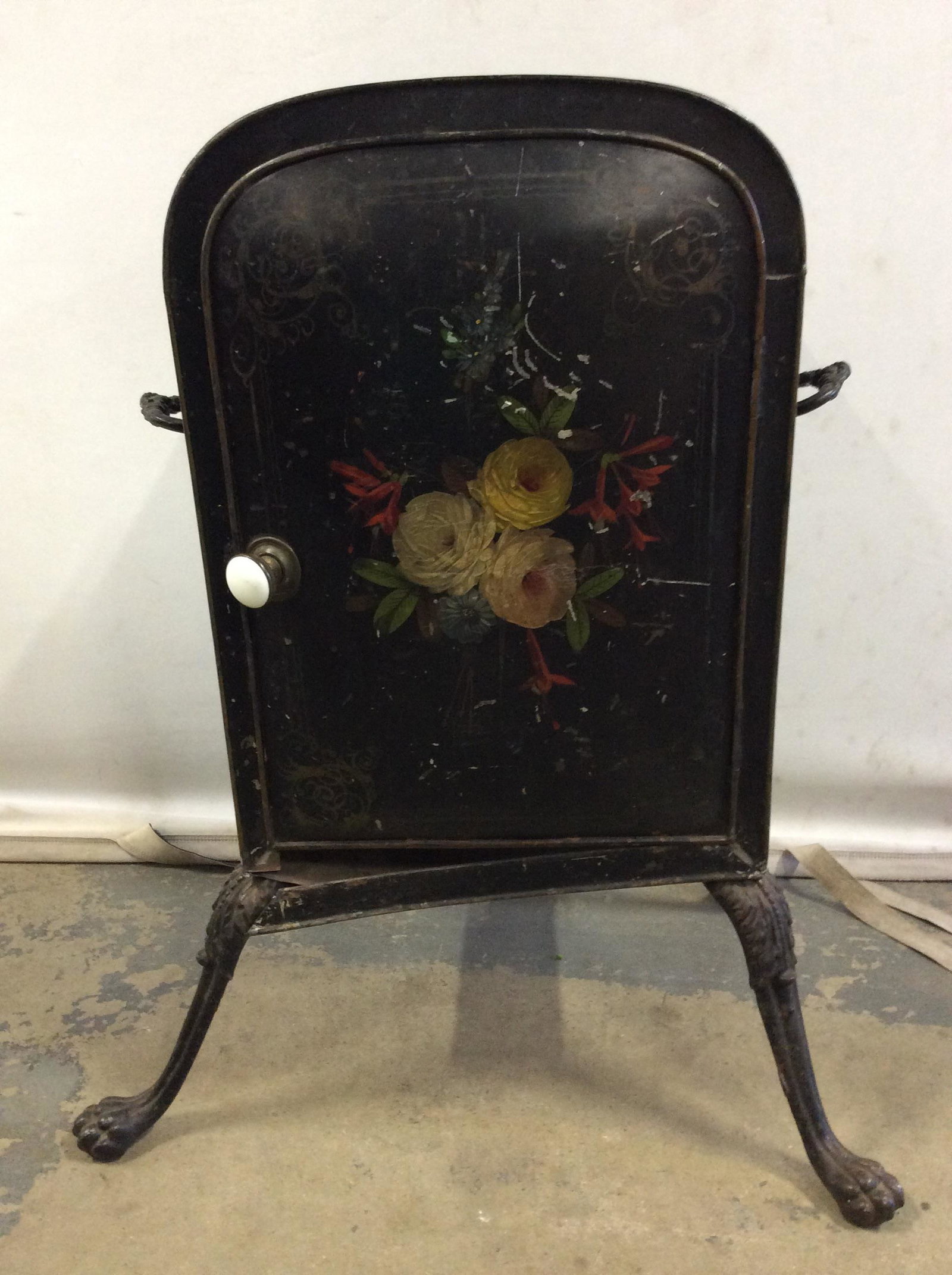 Antique Footed Metal Coal Bin: Coal bin is black toned and metal. Piece appears to be antique. Piece has multi toned floral & leaf detail. Piece is possibly hand painted. Bin has 2 handles & 2 interior shelves. Piece has door with