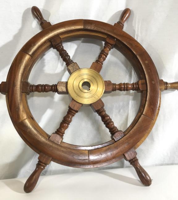 Nautical 24 in. 6 Spoke Teak Ship’s Wheel,: 24.5 in diameter. Possible Teak/ oak wood combo. Axle, née nave, made of brass w/ brass screws, felloes are attached with wooden rivets, flat to surface. Sturdy, heavy, minor surface scuffs. Carved h
