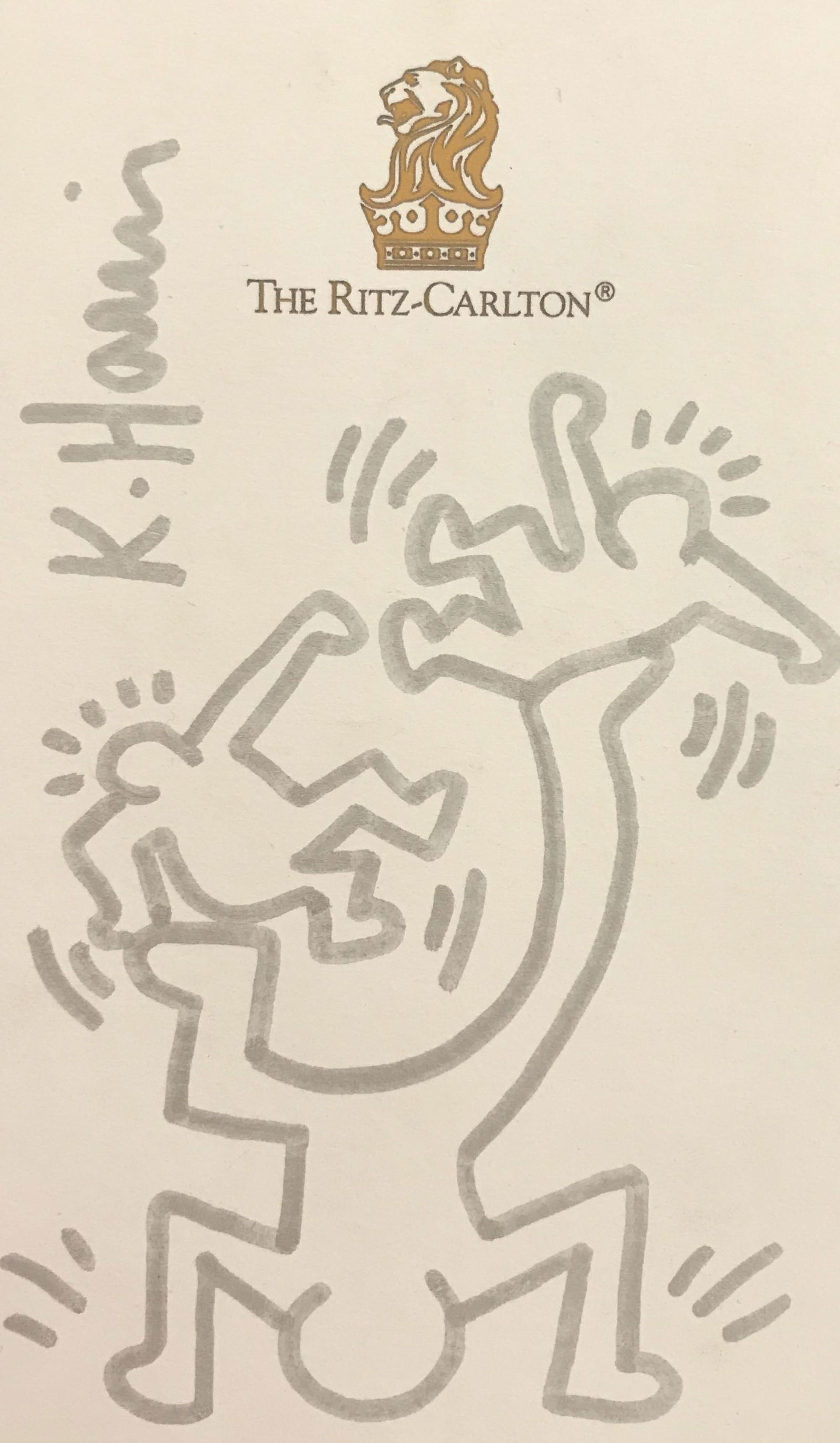 Signed Marker Drawing On Paper After Keith Haring: Appears to be a silver marker drawing on The Ritz Carlton note paper, three figures, two smaller figures balancing on larger figure’s feet, signed K. Haring vertically on upper left side of paper, u