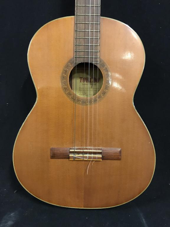 Six string Toredo Acoustic Guitar: Six string toredo acoustic guitar. Some loss present on piece. The piece measures approx. 39 inches H and 14.75 inches W, at its widest. Acoustic instrument, acoustic guitar, six string guitar. musica