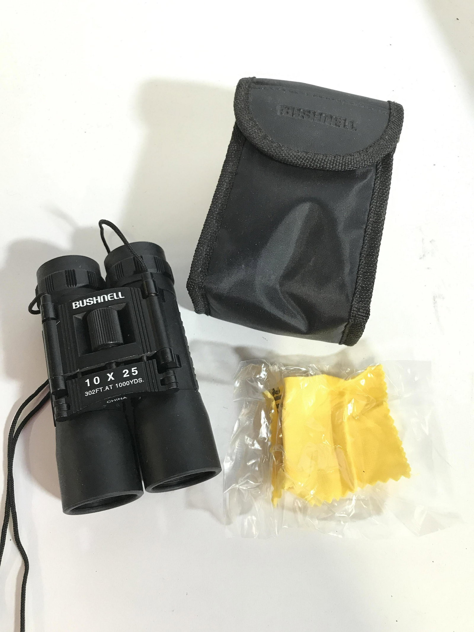 Bushnell Pocket Size Binoculars w/ Pouch: Binoculars 10 x25 / 302 FT at 1000 yards, measure 4.5 x 3 in. w/ attached neck string, hangs 18 in. Includes wipe cloth still in package and carry case w/ Velcro closure & backside carry handle. Case 