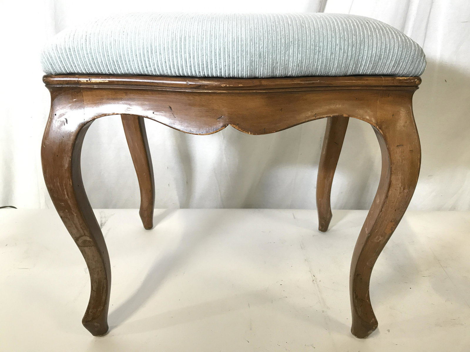 Vintage Upholstered Carved Wooden Footstool: Footstool is wooden with carved legs. Piece has light slate green toned upholstery. Piece measures approximately 20 inches tall and wide 16 inches deep. Footstool, Upholstered footstool, Vintage foots