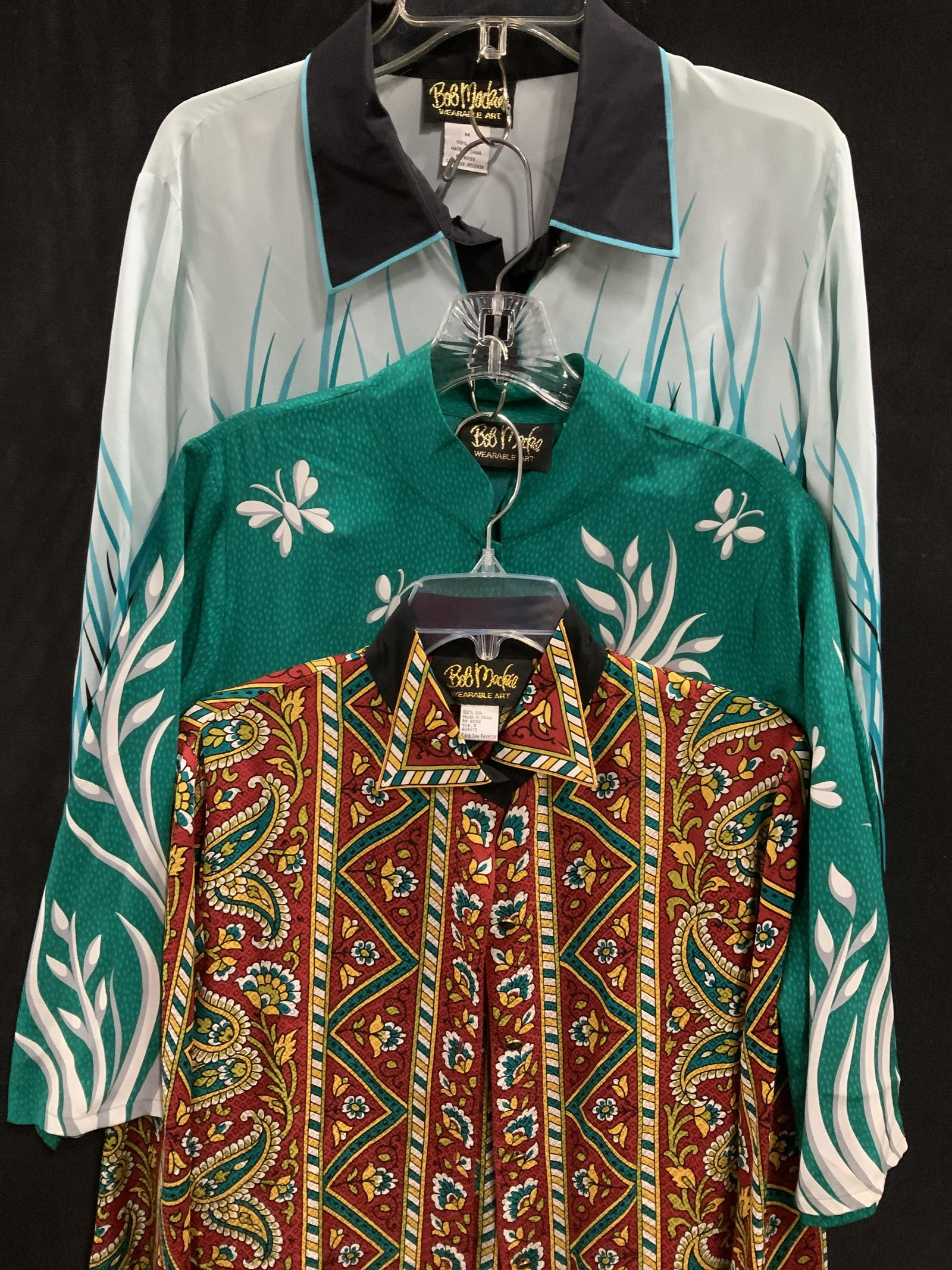Lot 3 Bob Mackie Ladies Long Sleeve Silk Blouses: Fashionable VINTAGE silk blouses in variety of patterns & colors. Size M and Small. From Bob Mackie’s high end ready to wearable Wearable Art Collection. All w/ side slits to tuck in. All with disti