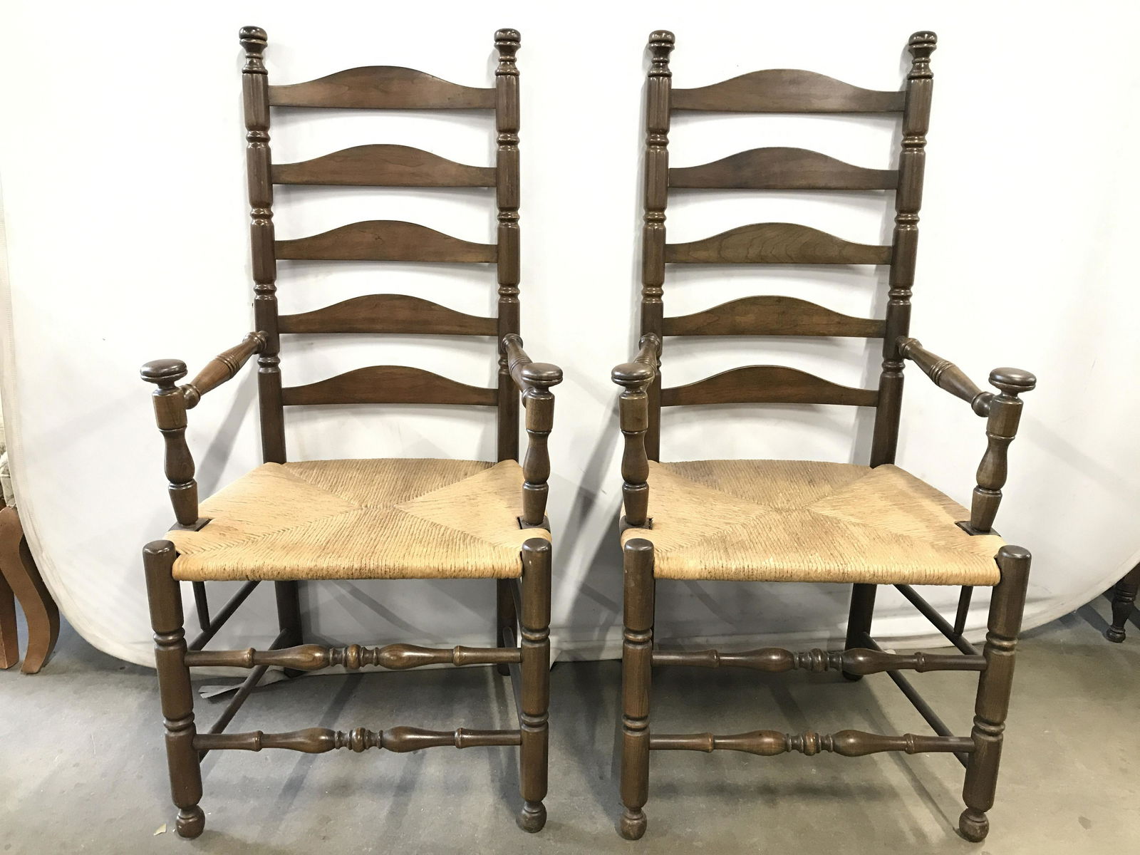Pair Carved Wooden Vintage End Chairs: Lot includes 2 chairs. Chairs have ladder backs and carved wooden detail. Chairs have Rush seats. Chairs have knob shapes at ends of armrests. Legs have stretchers. Chairs, end chairs, dining chairs,