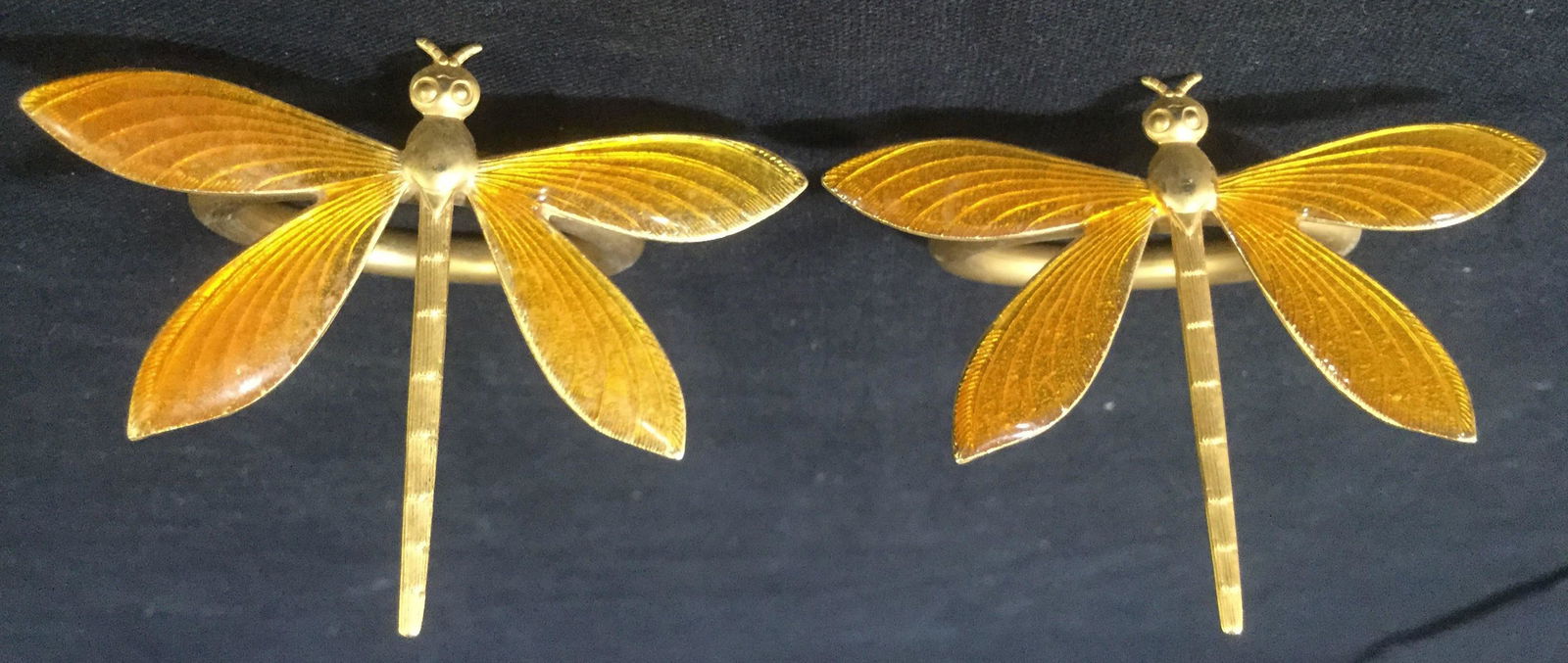 Set 7 Brass Dragonfly Napkin Rings: This lot includes 7 brass dragonfly shaped napkin rings. Several of the dragonfly wings are colored with orange enamel, one dragonfly has been colored with white enamel. The enamel has fallen off of t