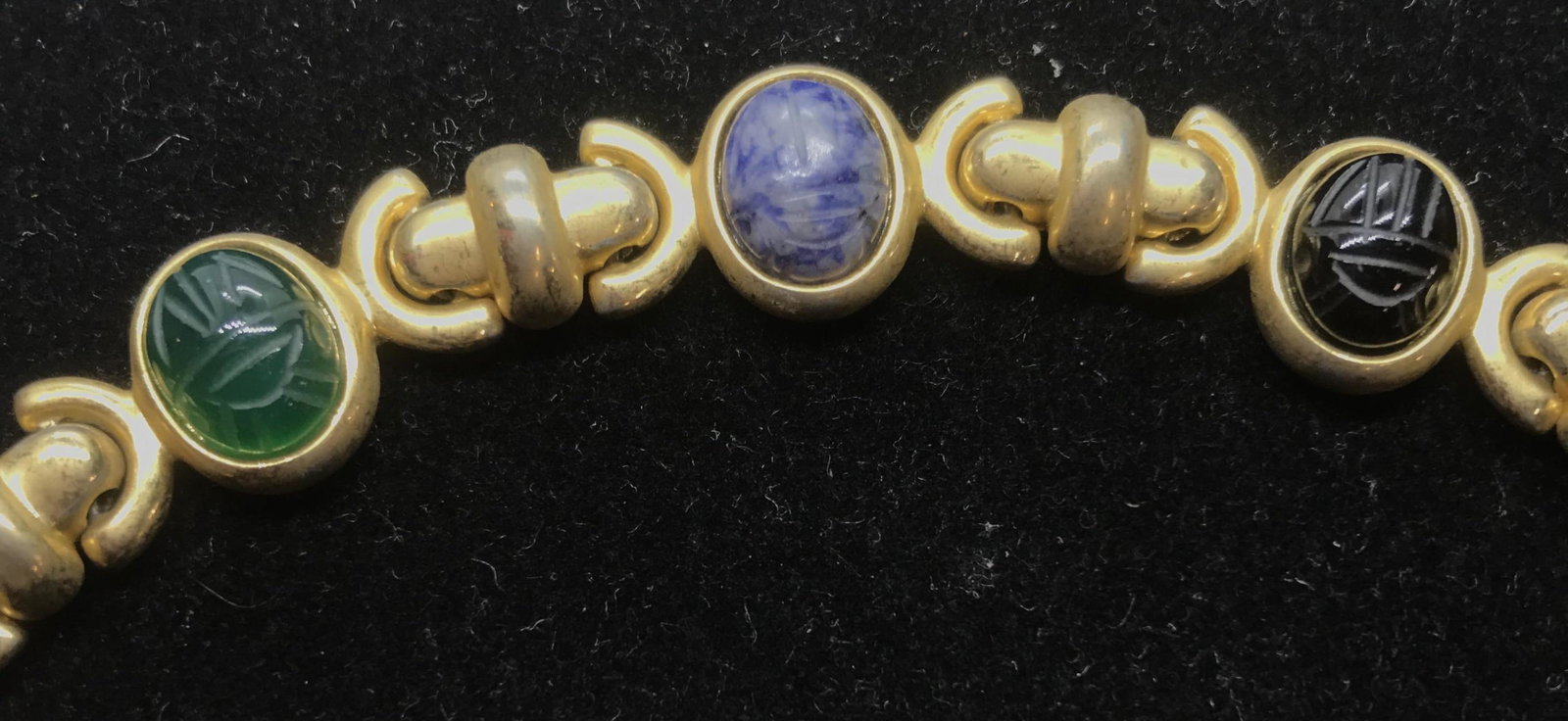 Multi Quartz Gem Cabochon Gold Tone Bracelet: Carved Natural Stone Oval cabochons, app 10x8 mm. Tests positive on gem tester for chrysoprase, onyx, carnelian, quartz. Secure latch. Labeled M in verso. 7.25 in. long. Metal has wear. Bracelet, Quar