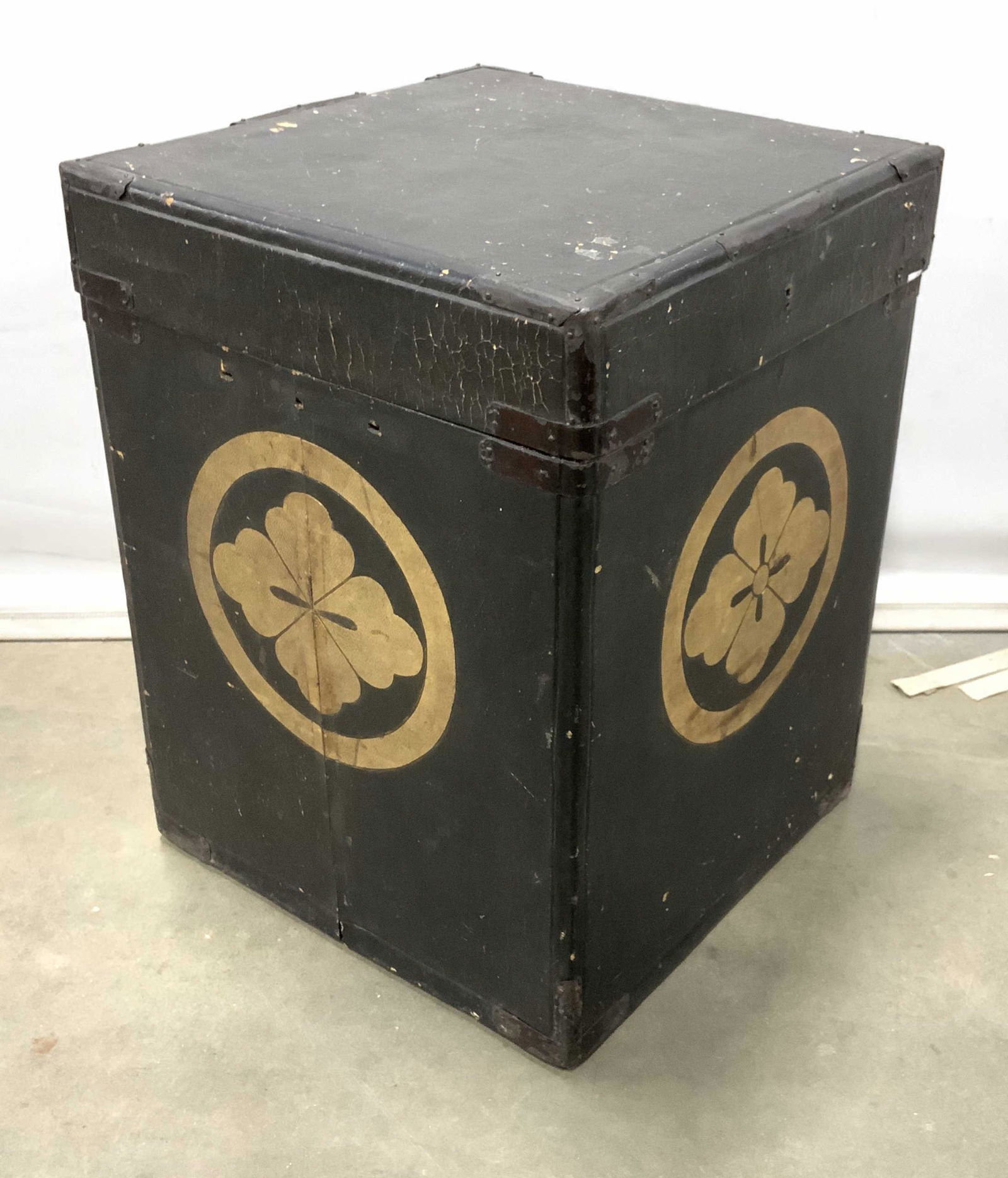 Antique Asian Styled Storage Box: This is an antique storage box. The piece is crafted from wood, and is bound in, what appears to be, leather. Gold toned flowers or insignias can be found on 3 sides of the box. A tag can be found on
