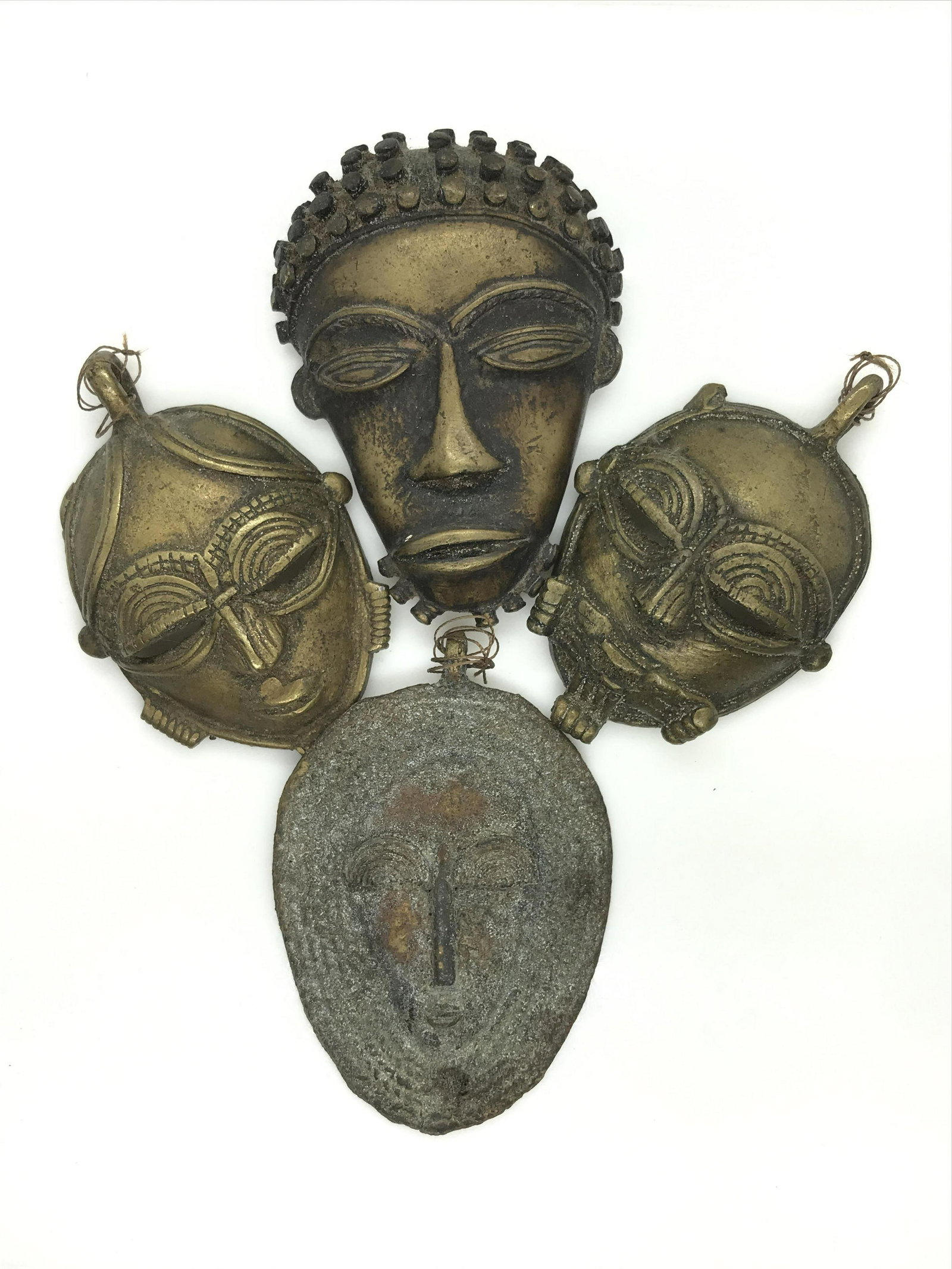Vintage Set 4 Bronze Tribal Face Figural Ornaments: Indo-Asian Facial Features on 2 of the bronze masks. Measure 3 x 2 in. Bail on top. 1 Has African Facial Features, measures 3 x2 in. Hole on top to hang on wall. Tribal face, has some wear to metal. M
