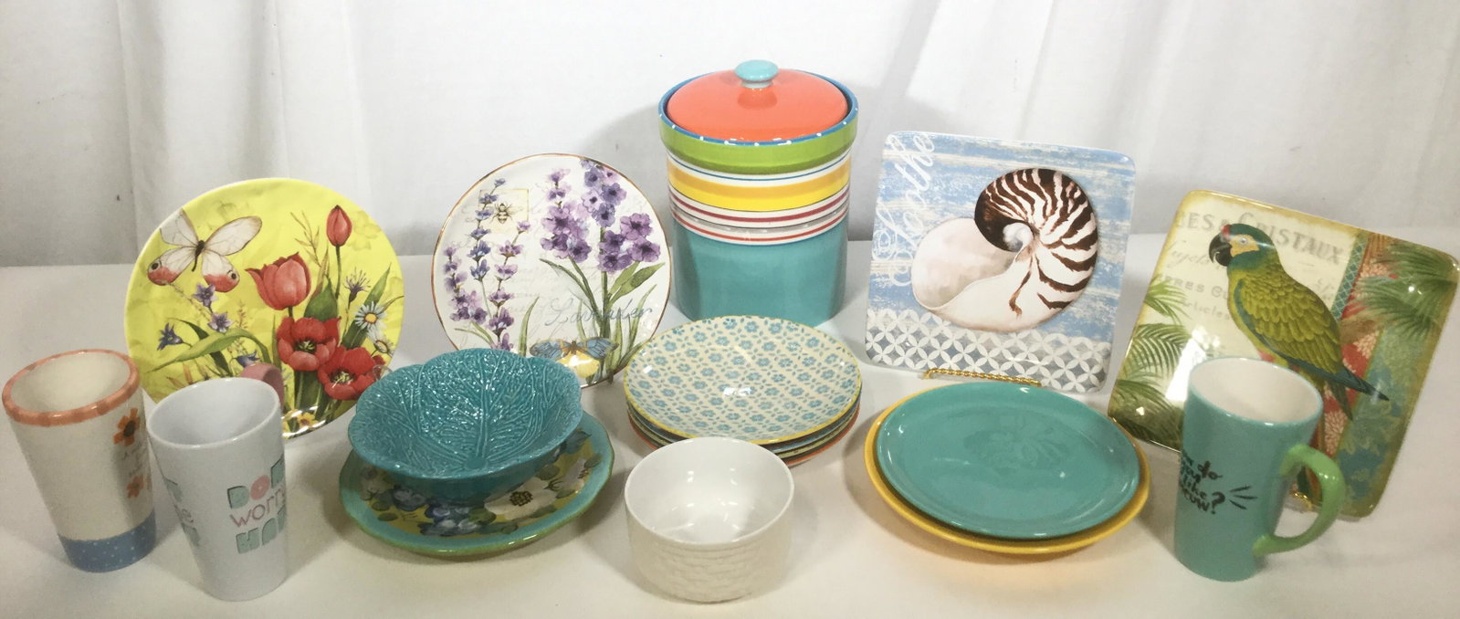 Lot 18 Assorted Spring Themed Dining Ware: This lot includes an assortment of spring and summer themed ceramic diningware. There are 4 cups, eleven dishes, two bowls, and a Cookie jar. The largest piece measures approx 8.5 inches H and 7.5 inc