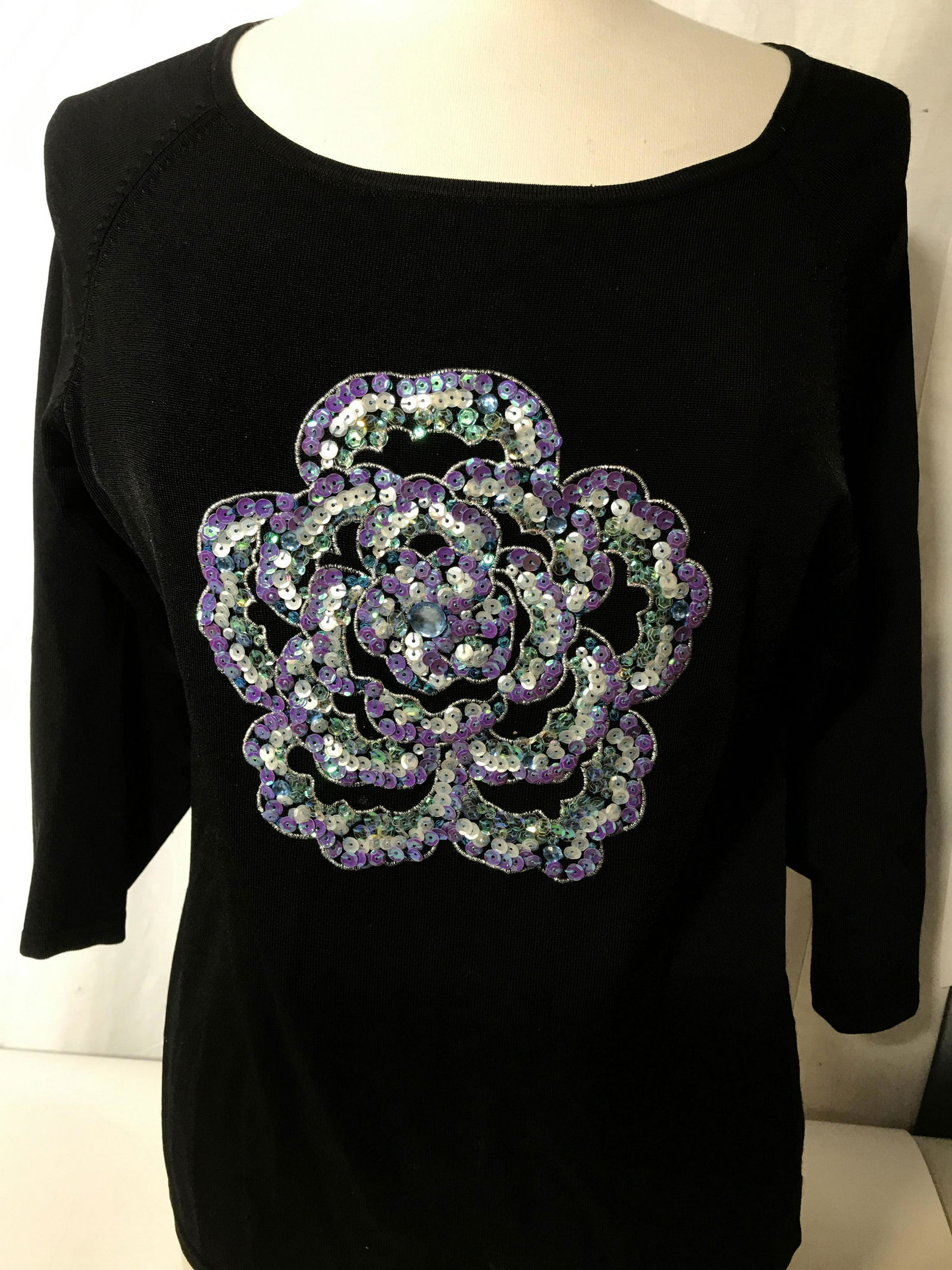 Victor Costa Blossom Sequin Black Spring Sweater: Size Med. 77% rayon, 22% Nylon. Large center sequin flower of purple & white rainbow sequins with silver thread embroidery. 7.5 in. diameter. Slight pull of thread on shoulder. Wide crew neck. Ladies