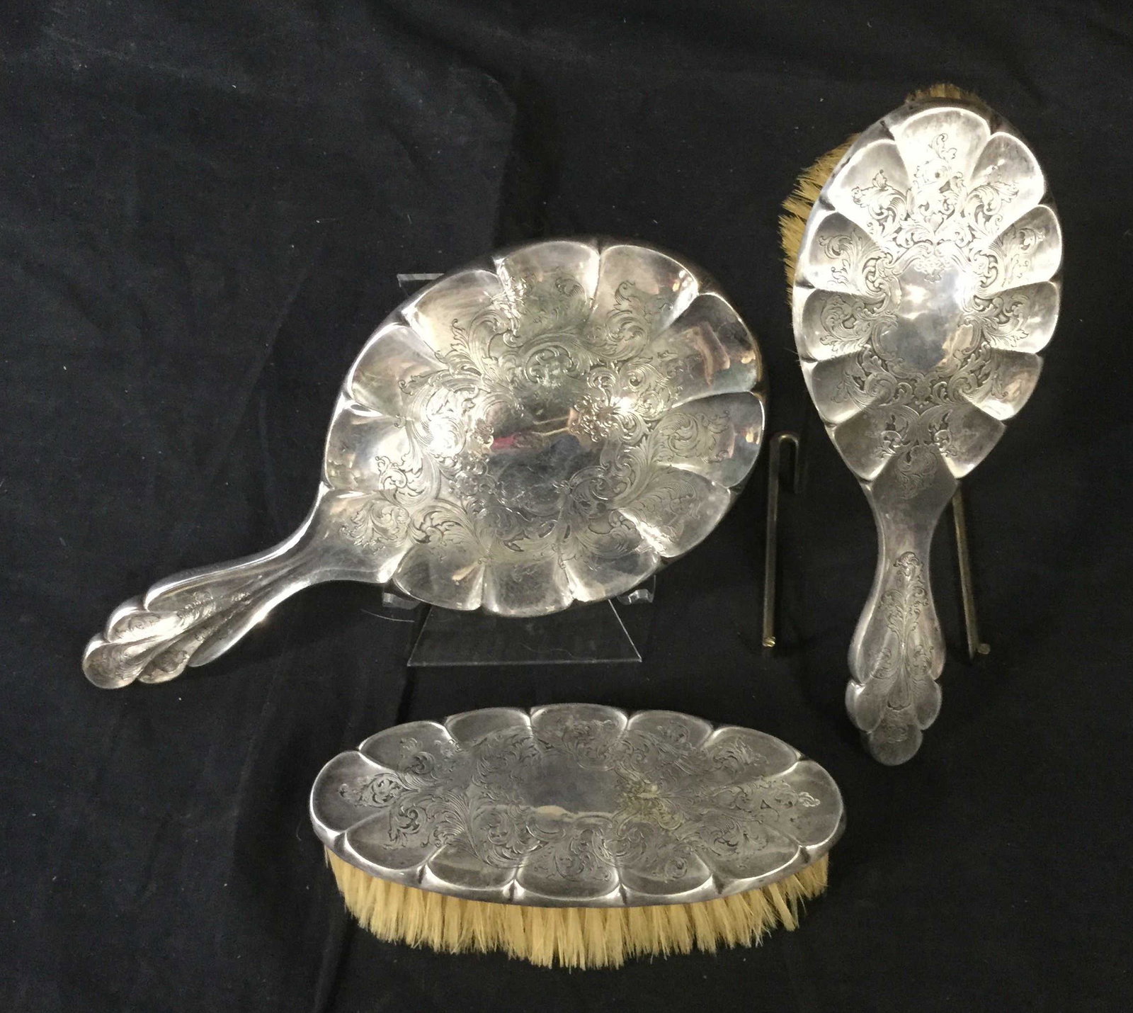 Antique Silver Toned vanity set: Antique silver toned vanity set including a hand mirror, a body brush and a hair brush. Each item has floritine carvings and scalloped edges. Largest item measures at 10 inches long and 5 inches acros