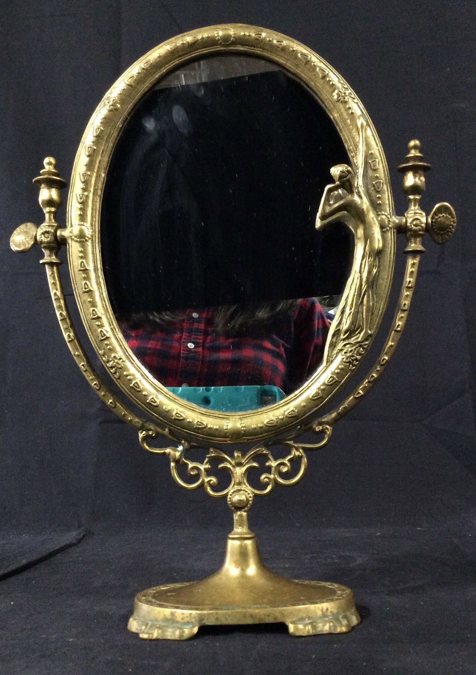 Antique Art Nouveau Brass Tilting Dresser Mirror: Antique Art Nouveau Brass Tilting Dresser Mirror with female figural peering into the mirror surrounded by intricate design on mirror border and pedestal base, reverse of mirror has red velvet backing