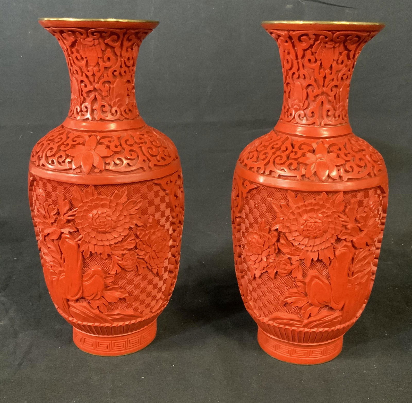 Pair Chinese Cinnabar Carved Vases: Vintage carved Chinese vases. Antique table top accessory. Red carved exterior. Traditional Peking carved lacquer. 10 inches tall. Carving depicts flower garden with copper ring around mouth and base